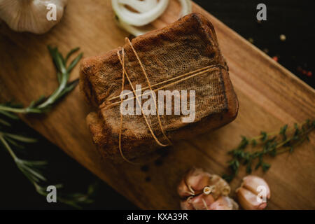 Klumpen von gesalzenem geräucherten Speck in Gaze mit einem Seil. Traditionelle russische und ukrainische Mahlzeit. Gesundes Essen mit pranami Gewürze, Kräuter, Zwiebel und Knoblauch. Stockfoto