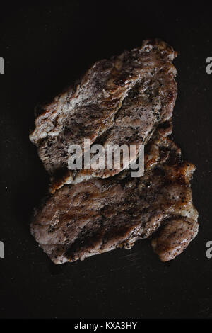 Essen Foto im rustikalen Stil. Gegrilltes Fleisch. Schweinesteak auf dunklen schwarzen Hintergrund von Schiefer. Ansicht von oben. Flach. Stockfoto