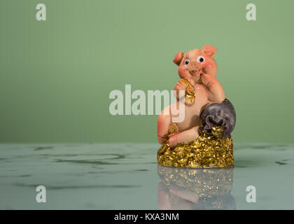 Figur eines kleinen Schweinchen sitzt auf einem Haufen von gold, grün Hintergrund Stockfoto