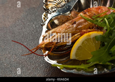 Eine gebratene Tiger Garnelen oder langostino mit Gruenen und Zitrone auf alten Platte auf dunklem Hintergrund. Nahaufnahme Stockfoto