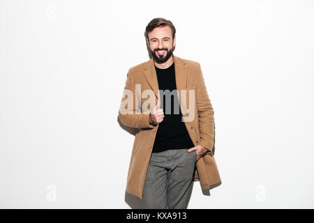 Porträt einer fröhlichen bärtigen Mann in einen Mantel ständigen gekleidet, und wenn man die Kamera auf weißem Hintergrund Stockfoto