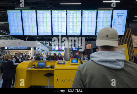 AMSTERDAM, NIEDERLANDE - 27.Dezember 2017: Ein Mann ist mit Blick auf die Informationsseiten seinen Flug am Flughafen Schiphol bei Amsterdam zu prüfen. Stockfoto