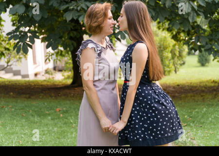 Closeup Portrait von erwachsenen Tochter und Mutter Natur. Hübsche Brünette und ihre Mutter sind auf der Suche in die Kamera im Park im Sommer Stockfoto