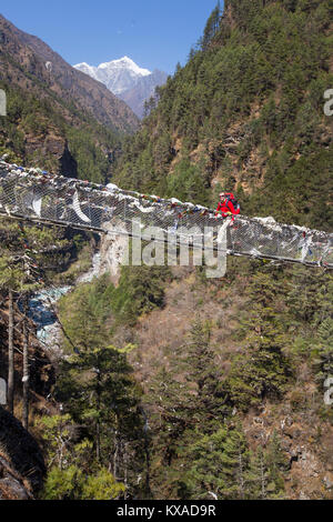 Ein solo Mann Wanderer ist das Überqueren einer Nepalesischen suspension Brücke über eine tiefe Schlucht auf dem Weg nach Namche Bazar. Stockfoto