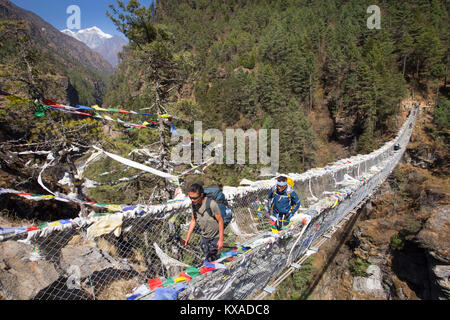 Zwei Wanderer sind Kreuzung einer nepalesischen suspension Brücke über eine tiefe Schlucht auf dem Weg nach Namche Bazar. Stockfoto