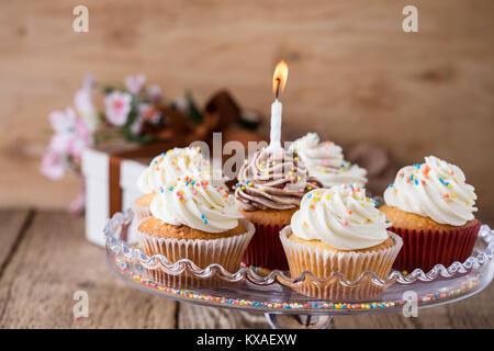 Lecker geburtstag Cupcakes mit einer Kerze serviert auf Glas cakestand auf festliche Holztisch Stockfoto