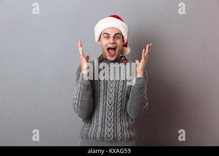 Foto der jungen schockiert emotionale Mann, weihnachten santa hut stehend über graue Wand isoliert. Suchen Kamera. Stockfoto