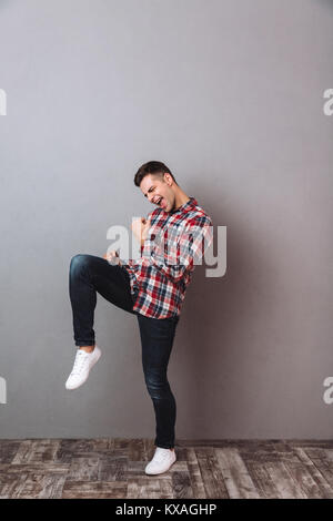 Volle Länge Bild von schreienden glücklicher Mann im Hemd und Jeans freuen über grauer Hintergrund Stockfoto