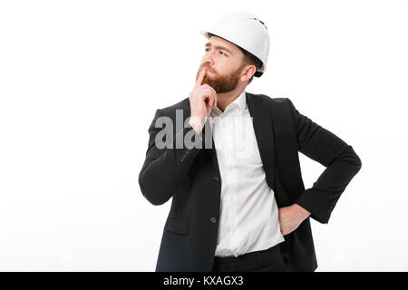 Nachdenklich bärtigen business Mann in Schutzhelm über weißen Hintergrund suchen Stockfoto