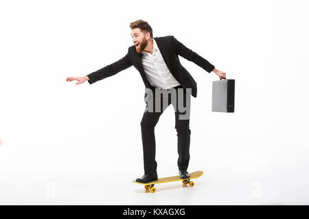 Volle Länge Bild von fröhlichen Bärtigen business Mann mit Aktentasche reiten auf Skateboard auf weißem Hintergrund Stockfoto