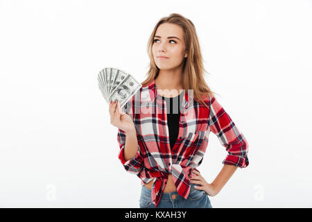 Porträt eines lächelnden hübsches Mädchen in Plaid Shirt holding Bündel geld Banknoten und entfernten Blick auf weißem Hintergrund Stockfoto