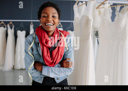 Portrait von afrikanischen Frauen Bridal store Inhaber stand mit verschränkten Armen und lächelnd. Frau Schneider, die in der Hochzeit Mode Shop.