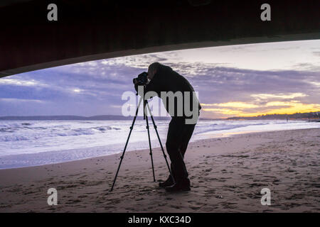 Silhouette eines männlichen Fotografen Fotografieren mit einem Stativ bei Sonnenuntergang, Bournemouth, England, Großbritannien Stockfoto