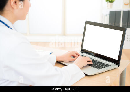 Ziemlich elegante Frau Doktor über mobile Laptop eingeben Arbeiten in Klinik Büro mit weißen leeren Bildschirm. selektive Fokus Foto. Stockfoto