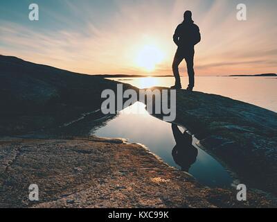 Silhouette Mann auf einer Klippe über dem Meer. Touristische stand alone auf einem Felsen und Meer Horizont Sonnenuntergang. Wanderer die Spiegelung in der Nähe Wasser Pool. Stockfoto