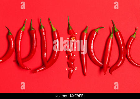 In Scheiben geschnittene Chilischote Pfeffer auf einem roten Hintergrund angeordnet Stockfoto