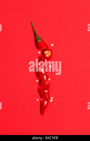 In Scheiben geschnittene Chilischote Pfeffer auf einem roten Hintergrund angeordnet Stockfoto