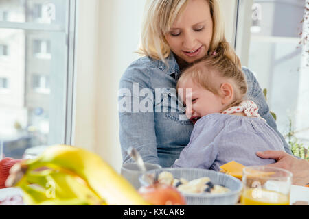 Kleines Mädchen weinend in den Armen Mutter am Frühstückstisch Stockfoto