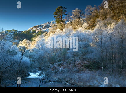 Wasserfall im Winter mit einem schneebedeckten Ben Venue und Bäume im Raureif im Hintergrund abgedeckt. Stockfoto