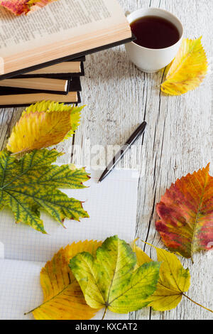 Offenes Buch und Notebook mit einem Kugelschreiber, Tasse und Herbstlaub auf einem weißen Holz- Hintergrund Stockfoto