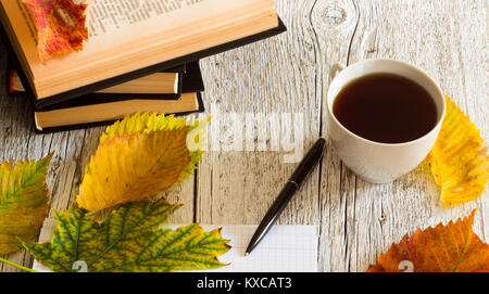 Offenes Buch und Notebook mit einem Kugelschreiber, Tasse und Herbstlaub auf einem weißen Holz- Hintergrund Stockfoto