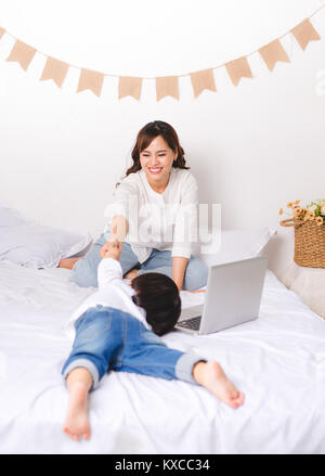 Junge asiatische Mutter arbeiten, während ihr Baby Girl auf Boden zu Hause sitzen. Stockfoto