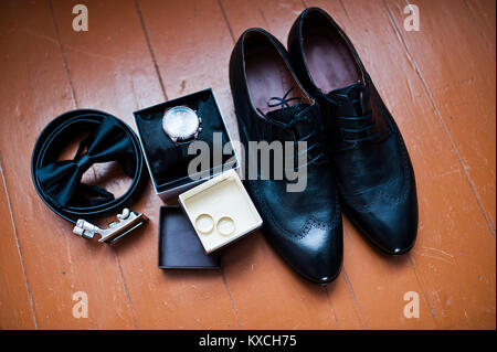 Nahaufnahme der schwarz Bräutigam brogue Schuhe, Uhren, Trauringe, Riemen und Bow Tie auf dem hölzernen Hintergrund. Stockfoto