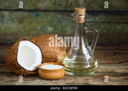 Frische ganze und halbierte Kokosnüsse mit Kokosöl und Flocken auf hölzernen Hintergrund mit Kopie Raum Stockfoto