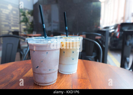 Iced Mokka und Iced Latte Kaffee Getränke in Plastikbecher mit Strohhalmen auf Holz Tisch draußen ein Cafe. Stockfoto