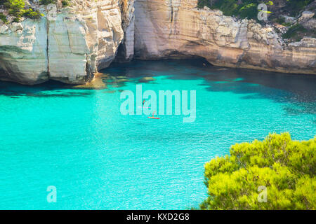 Menschen paddleboarding auf dem smaragdgrünen Wasser von Cala Mitjana, Menorca, Balearen, Spanien Stockfoto