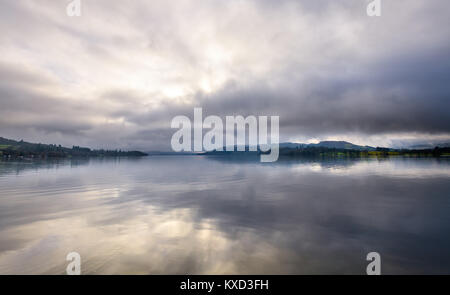 In Windermere Holme Crag, Waterhead, Ambleside wie die frühen Morgennebel löscht mit dramatischen cloud Reflexionen Stockfoto