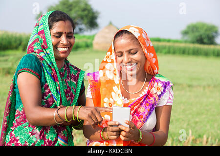 2 Indischen ländlichen Damen Lesen von Text Nachricht Telefon Bauernhof genießen. Stockfoto