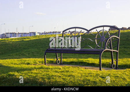 Ein pulverbeschichtetem Metall Parkbank in zeitgenössischem Design mit Hintergrundbeleuchtung mit dem weichen Licht der Wintersonne Stockfoto