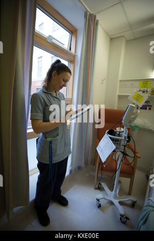 Stationsschwester Charlotte Howden, Eingabe von Daten in ein iPad auf einer Gemeinde in Whiston Hospital in Merseyside. Das Gerät wird verwendet, um die elektronischen Geänderte Frühwarnsystem (EMEWS), die hilft, alert klinische Personal an die Patienten bevorzugte Behandlung im Krankenhaus erfordern, zu erleichtern. Das System, an Whiston Hospital im Jahr 2016 eingeführt wurde, können die Mitarbeiter zu überwachen und die Versorgung der Patienten Effizienter regulieren als bisherige Papier-basierten Systemen. Stockfoto