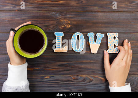Weibliche Hände mit Kaffee und herzförmige Plätzchen auf Holztisch, Ansicht von oben. Liebe Konzept. Cookies Liebesbrief. Stockfoto