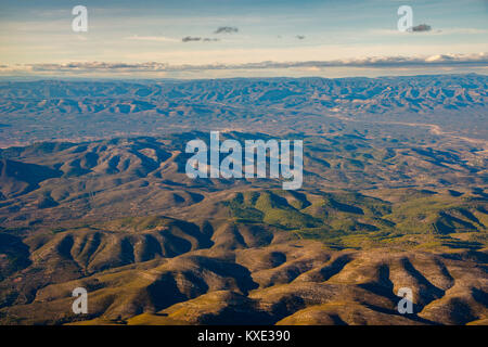 Blick aus dem Flugzeug auf sanften Hügeln bei Sonnenuntergang. Felsen, Wald und Horizont sichtbar. Stockfoto