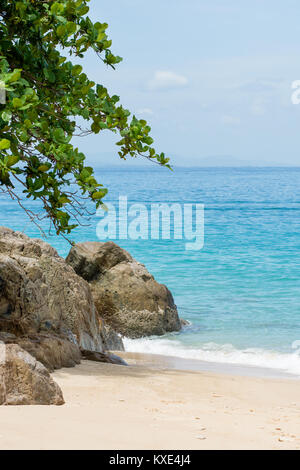 Gesunden grünen Baum Überhänge Schattierungen großen Felsen am Paradise White Sand Beach, ruhige türkisfarbene Meer und Horizont. Stockfoto