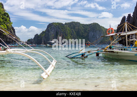 Philippinische Pumpe Boote an einem sonnigen Tag landete an Land auf einem weißen Sandstrand mit einer Kulisse von mehr Boote auf dem Meer und Baum bedeckt vulkanische Felsen und Stockfoto