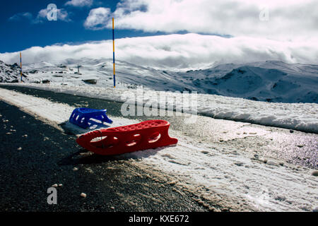 Schlitten. Zwei Schlitten, Rot und Blau, auf einer verschneiten Straße. Stockfoto