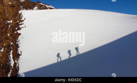 Schatten der Person auf einer senkrechten Felswand. Silhouette von Menschen klettern in überhängenden Klippe hoch über Wolken und Berge, Sonne, schöne bunte Himmel und Wolken hinter Stockfoto