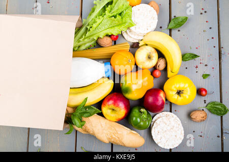 Einkaufen Konzept. Verschiedene Lebensmittel in Papiertüte auf Holz- Hintergrund. Flach Stockfoto