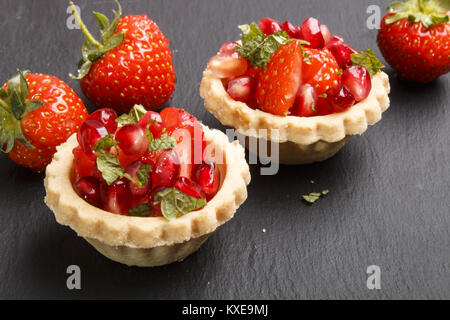 Törtchen gefüllt mit Erdbeeren, Granatapfel Saatgut und Minze auf Schiefer Stockfoto
