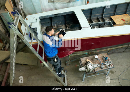 Hohen winkel Portrait von modernen digitalen Tablet während der Reparatur boot Yacht workshop Arbeiter, Kopie Raum Stockfoto
