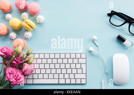 Blick von oben auf die Tastatur, Macarons, Brillen, Ohrhörer und Blumen isoliert auf Blau Stockfoto