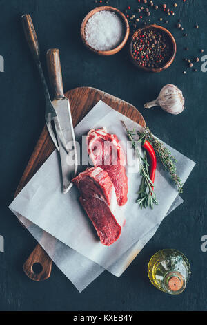 Ansicht von oben von rohem Fleisch Schichten auf parchent Papier- und Schneidebrett mit Besteck Stockfoto