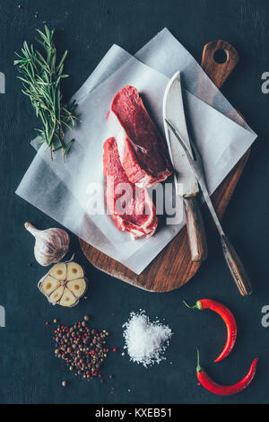 Ansicht von oben von rohem Fleisch Schichten auf parchent Papier- und Schneidebrett mit Besteck und Gewürze Stockfoto