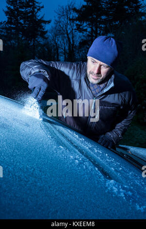 Ein Mann Eis kratzen von einem Auto Windschutzscheibe. Stockfoto