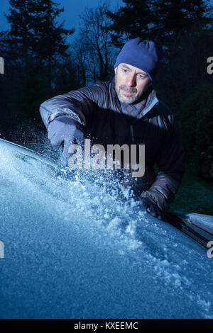 Ein Mann Eis kratzen von einem Auto Windschutzscheibe. Stockfoto