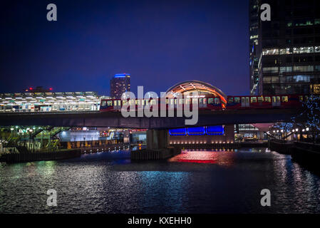 Die Docklands Light Railway Bahn über eine Brücke am Bahnhof in Canary Wharf in Wasser in der Nacht in den Docklands, London, England, UK wider Stockfoto