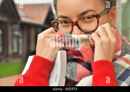 Porträt von einem asiatischen Mädchen in Gläser, Sie eingeschraubt ihr Gesicht mit einem Schal, nur die Augen und die Hände sichtbar sind. Das Haar ist der Knoten gebunden. Ständigen o Stockfoto